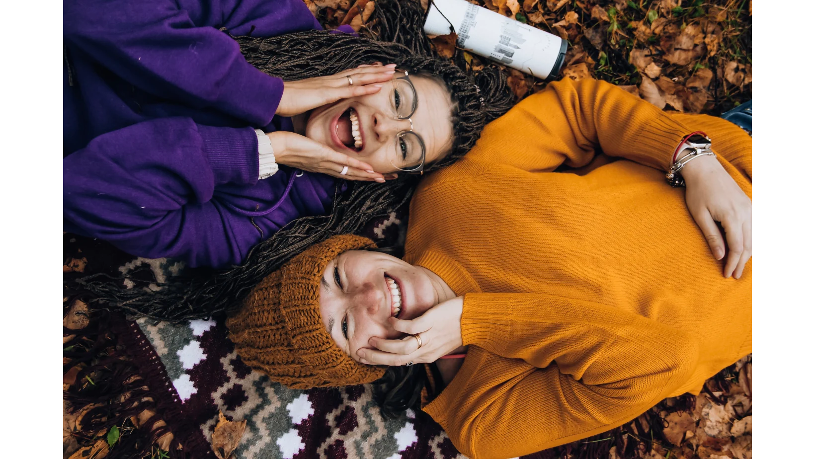 Two friends smiling together among autumn leaves
